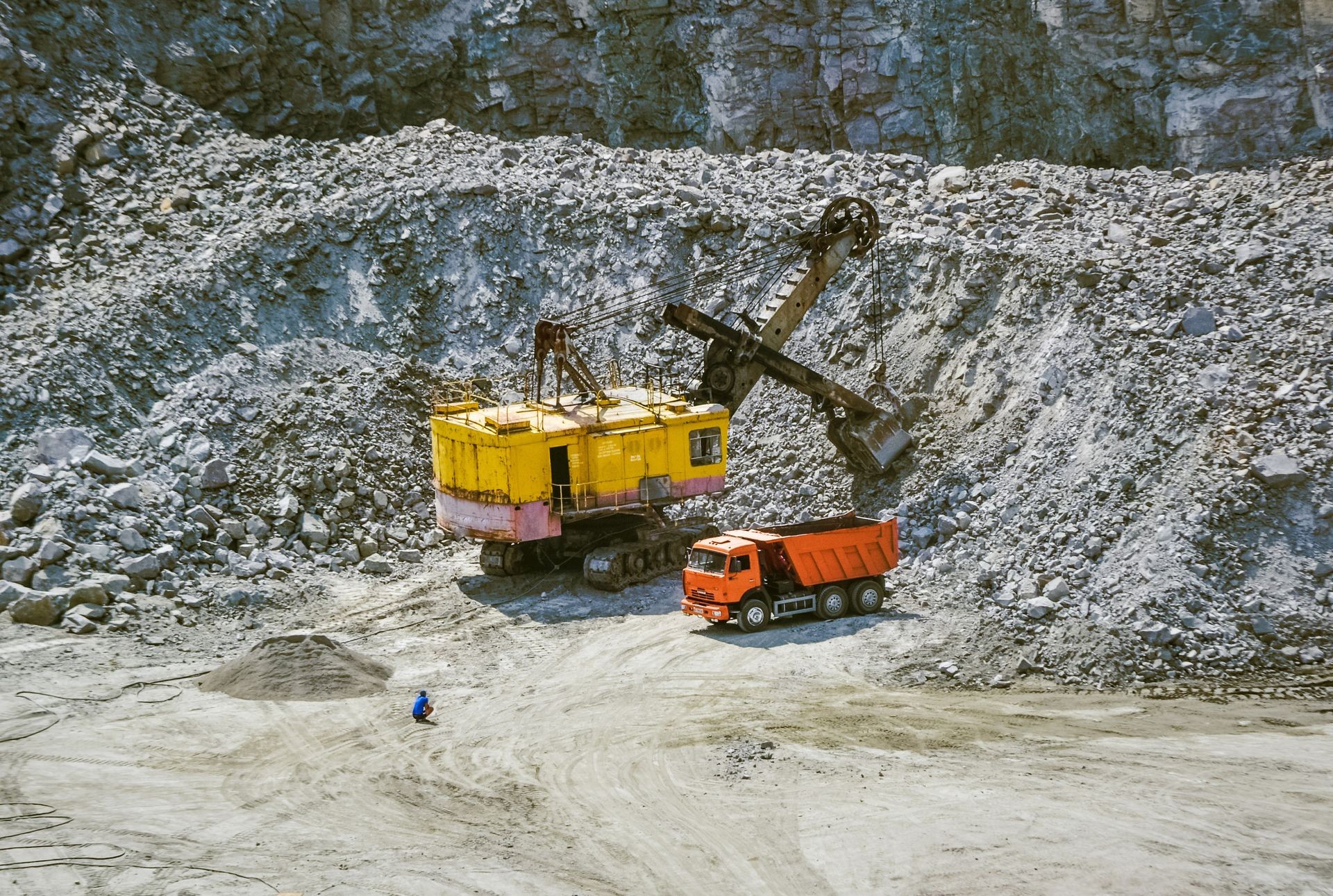 Huge excavator, truck and man standing next on granite quarry. Yellow carver machine, excavator, stonecutter for industrial granite stands in a quarry near granite stones