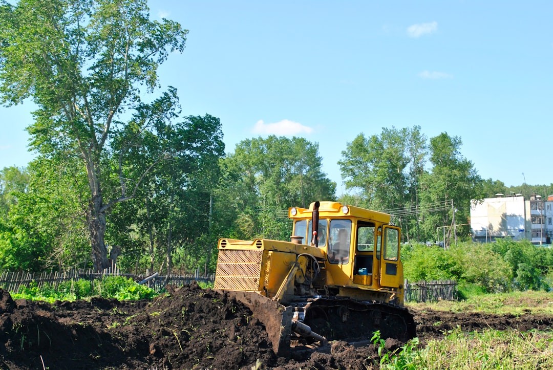 a bulldozer digging through a field with trees in the background